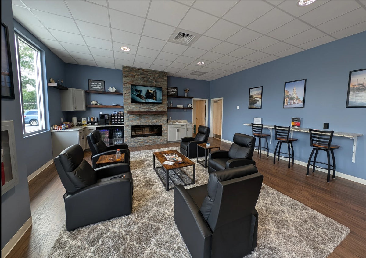 modern turbo tint lounge area with black leather recliners and bar stools, a stone fireplace with a mounted TV, wood floors, blue walls, and a patterned area rug for one hour window tint with complimentary food and drinks 